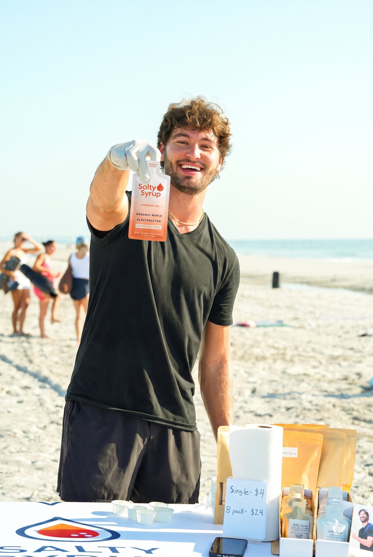Billy Bates holding up a Salty Syrup packet at a beach tasting table